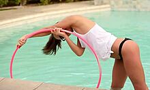 glasses-wearing teen gf with ponytail poses playfully with hula hoop in pool.