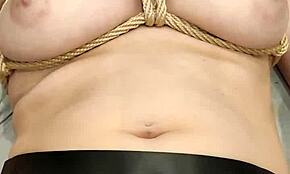 A woman gets tied up and uses a magic wand to reach orgasm at home.